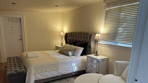 Een slaapkamer met een bed, nachtkastjes, een bankje en een raam met jaloezieën.
