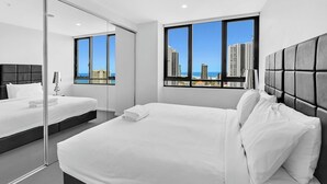 Una habitación de hotel moderna con una cama grande, una cama más pequeña y un separador de vidrio.