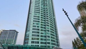 A tall, curved skyscraper with a glass facade, surrounded by palm trees and a pool area.