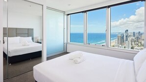 A modern hotel room with a large bed, a separate sleeping area, and a city view through large windows.