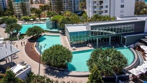 A modern hotel with a pool area, surrounded by tall buildings and greenery.