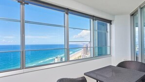 A balcony with a view of the ocean and beach, featuring a table and two chairs.
