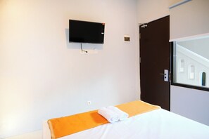 A hotel room with a bed, a TV mounted on the wall, and a window with a view of a building. - Djuragan Kamar Balawan (Malang)
