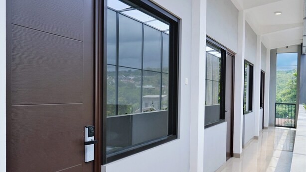 A corridor with sliding doors and windows, leading to balconies with views of greenery. - Djuragan Kamar Balawan (Malang)