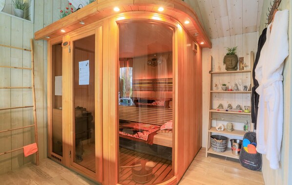A sauna room with a wooden interior, a glass door, and a shelf with towels and small Buddha statues.