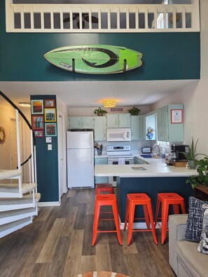 Une cuisine moderne avec des appareils électroménagers blancs, un îlot central et des tabourets orange vif.