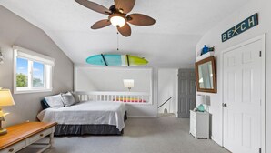A bedroom with a bed, a ceiling fan, a surfboard, a dresser, a mirror, and a door. - Spacious 2 Bedroom Condo in North Ocean City! (Ocean City)
