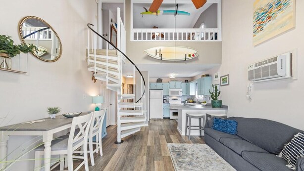 A modern apartment with a staircase leading to a loft, a dining area, and a living room with a sofa and a coffee table. - Spacious 2 Bedroom Condo in North Ocean City! (Ocean City)