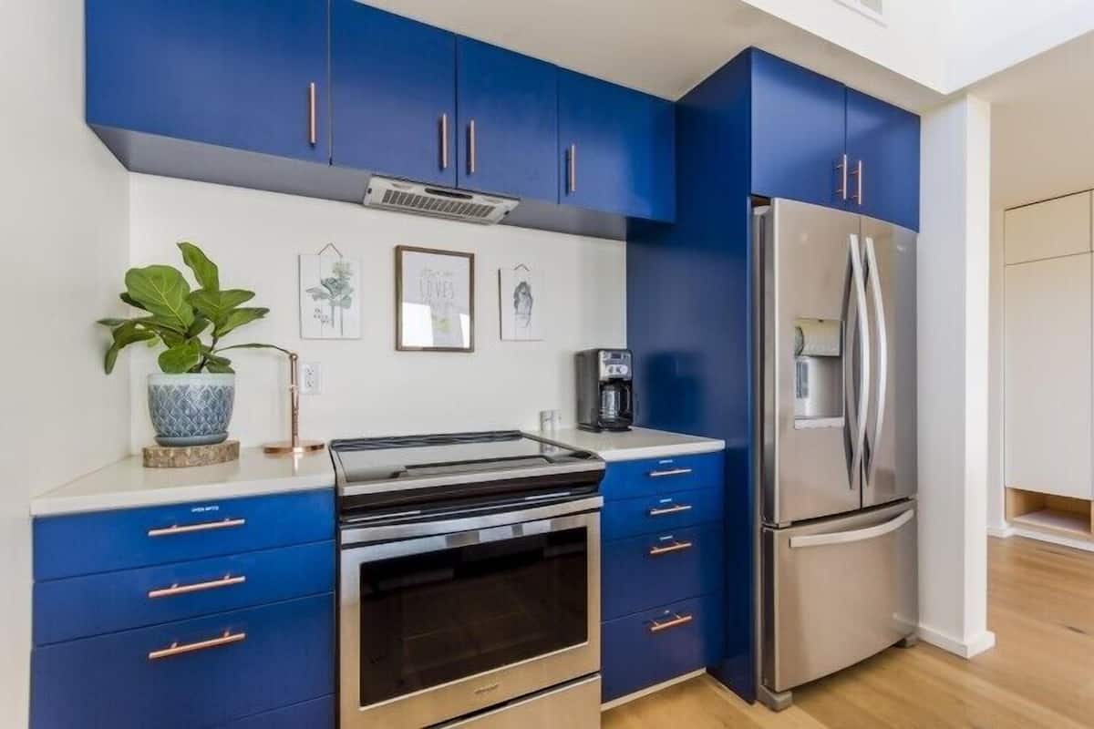 A modern kitchen with blue cabinets, stainless steel appliances, and a coffee maker.