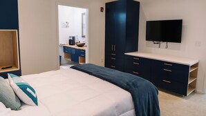 Ein Schlafzimmer mit Bett, Kommode, Fernseher und einem durchgehenden Türspalte sichtbaren Badezimmer.