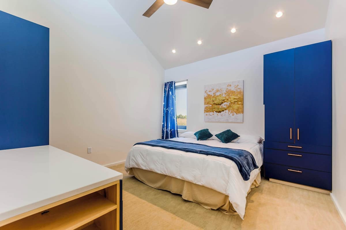 A bedroom with a bed, a desk, a wardrobe, and a ceiling fan.