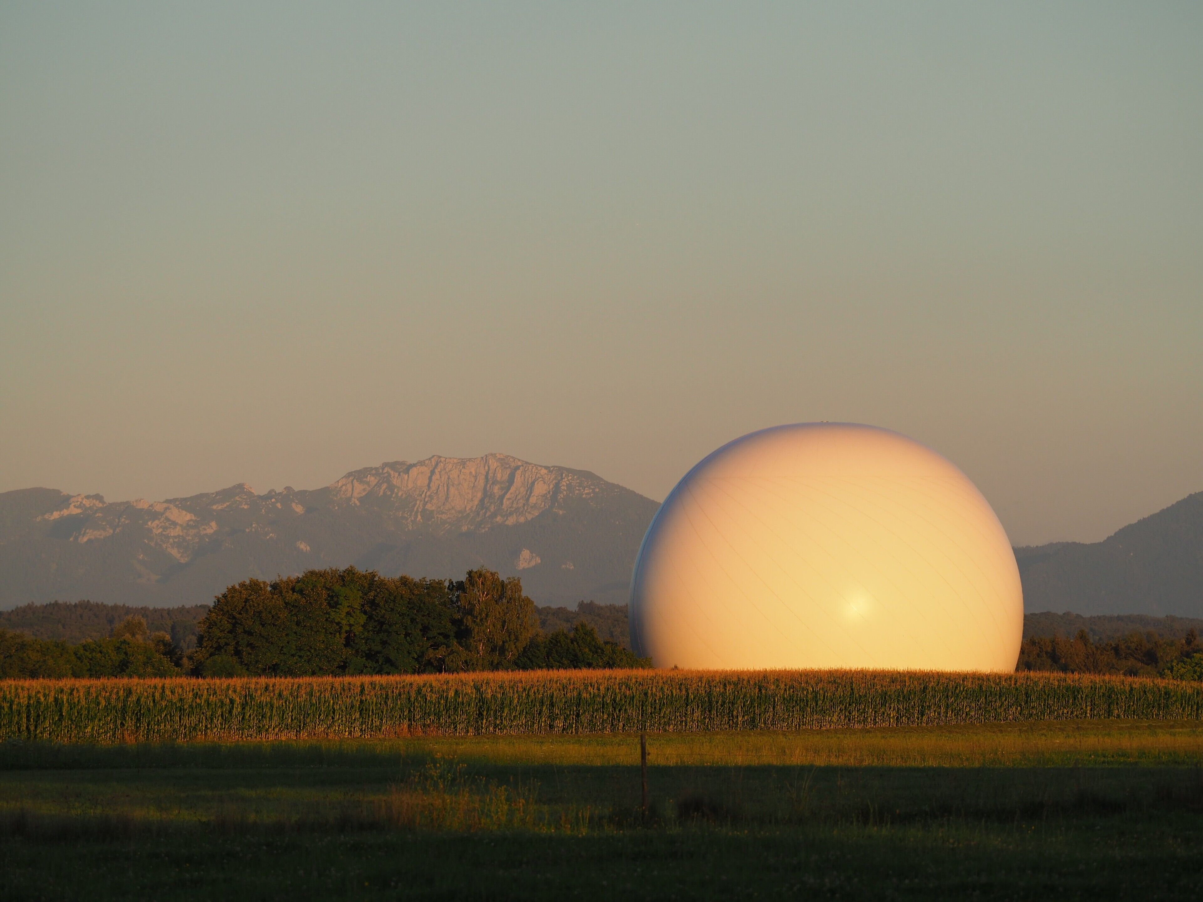 Un grand objet sphérique se trouve dans un champ, avec des montagnes en arrière-plan.