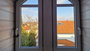 Une pièce avec deux fenêtres, des murs en bois et une vue sur les maisons voisines.