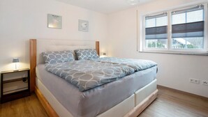 A bedroom with a bed, bedside tables, a window with blinds, and wall-mounted artwork.