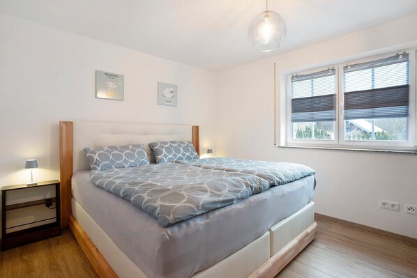 A bedroom with a bed, bedside tables, a window with blinds, and wall-mounted artwork.