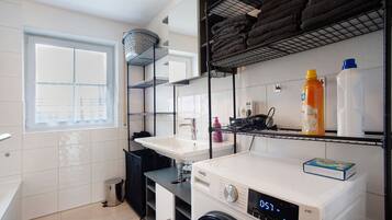 A laundry room with a washing machine, a sink, and shelves with towels and cleaning supplies.