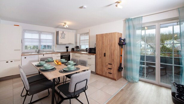A modern kitchen with a dining table, chairs, and a view through a glass door.