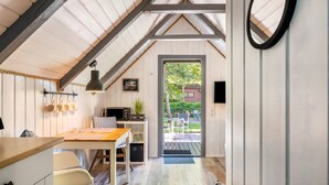 A cozy room with a wooden ceiling, a dining table, a chair, a small kitchen area, and a door leading outside.