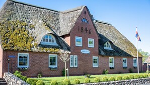 A brick building with a thatched roof, a stone wall, and a flag.
