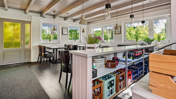 A kitchen with wooden beams, a bar area with stools, and a view of greenery outside.