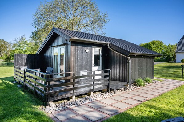 A modern wooden cabin with a deck, a window, and a door.