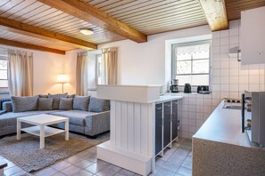 A modern kitchen with a built-in stove, a white countertop, and a dining area with a sofa and a coffee table.