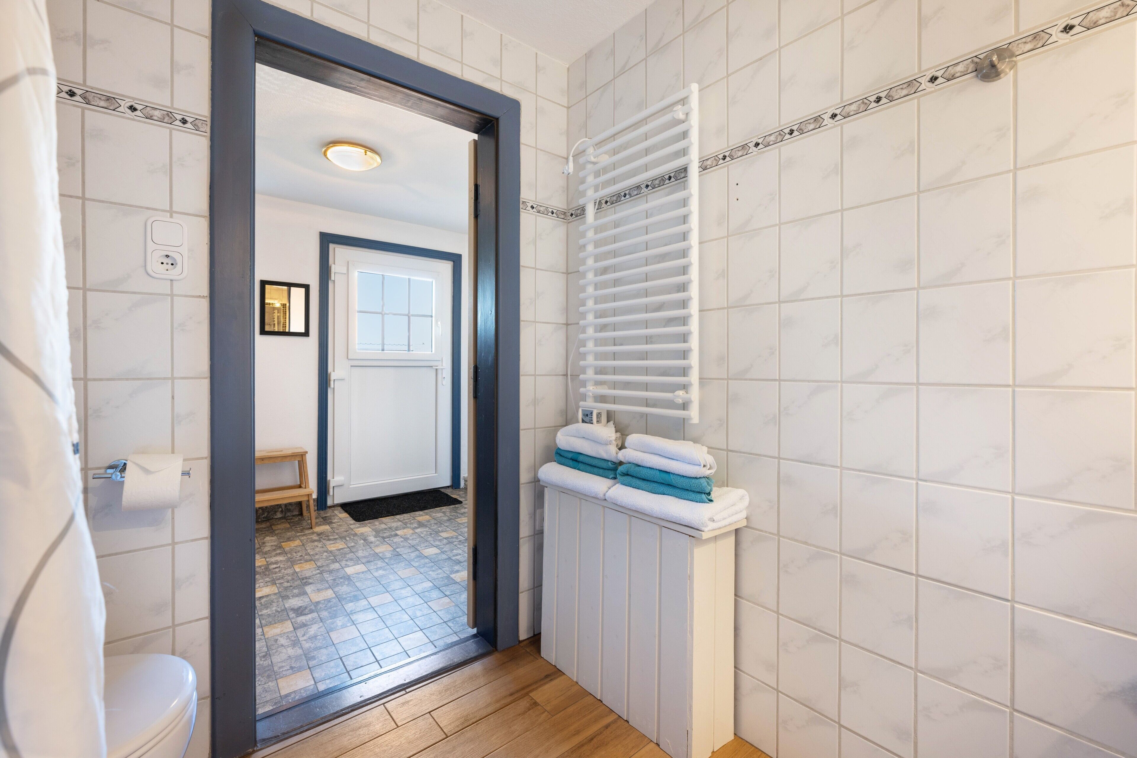 A bathroom with a toilet, a towel rack with towels, a shower area, and a tiled floor.