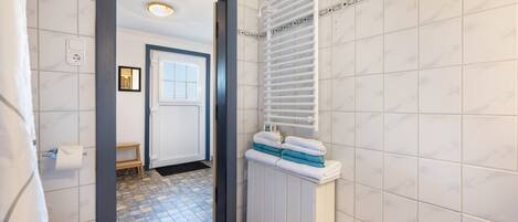 A bathroom with a toilet, a towel rack with towels, a shower area, and a tiled floor.