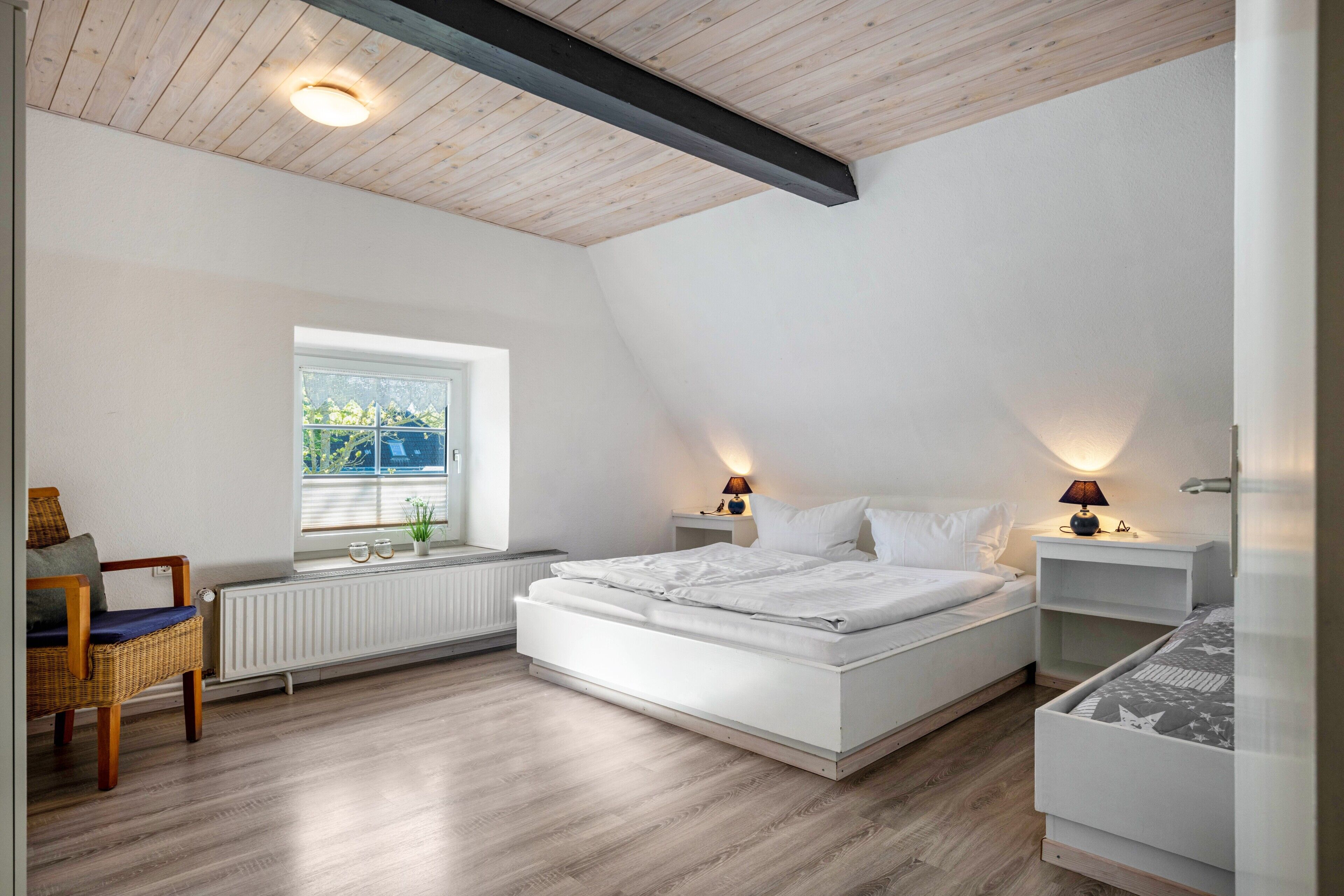 A bedroom with a sloped ceiling, a large bed, bedside tables with lamps, a chair, and a window with a view.