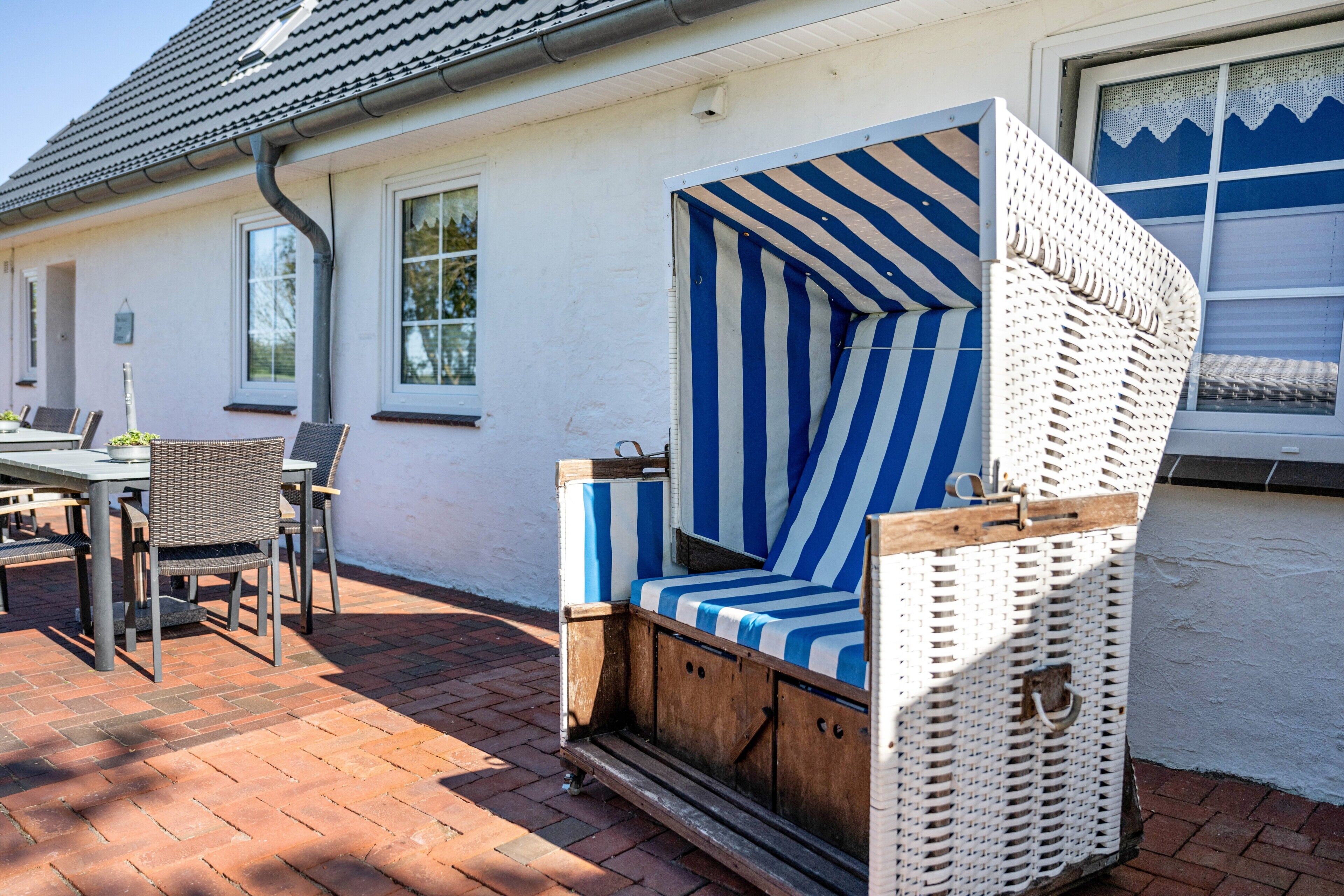 Ein Korbstuhl mit blauen und weißen Streifen, ein Tisch mit Stühlen und eine Terrasse mit Backsteinen.