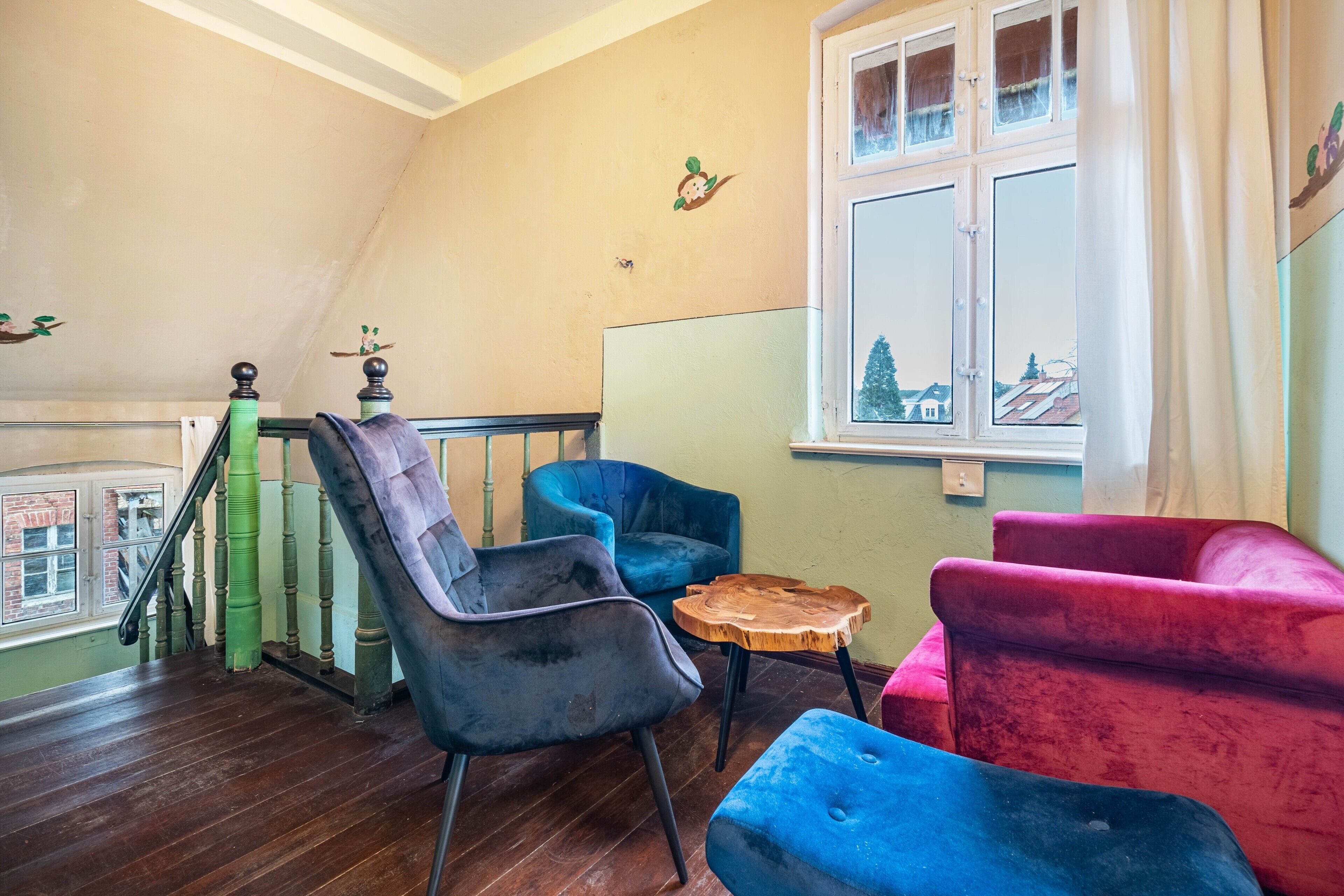 Ein Zimmer mit einer Holztreppe, einem Fenster mit Blick und drei Polsterstühlen.