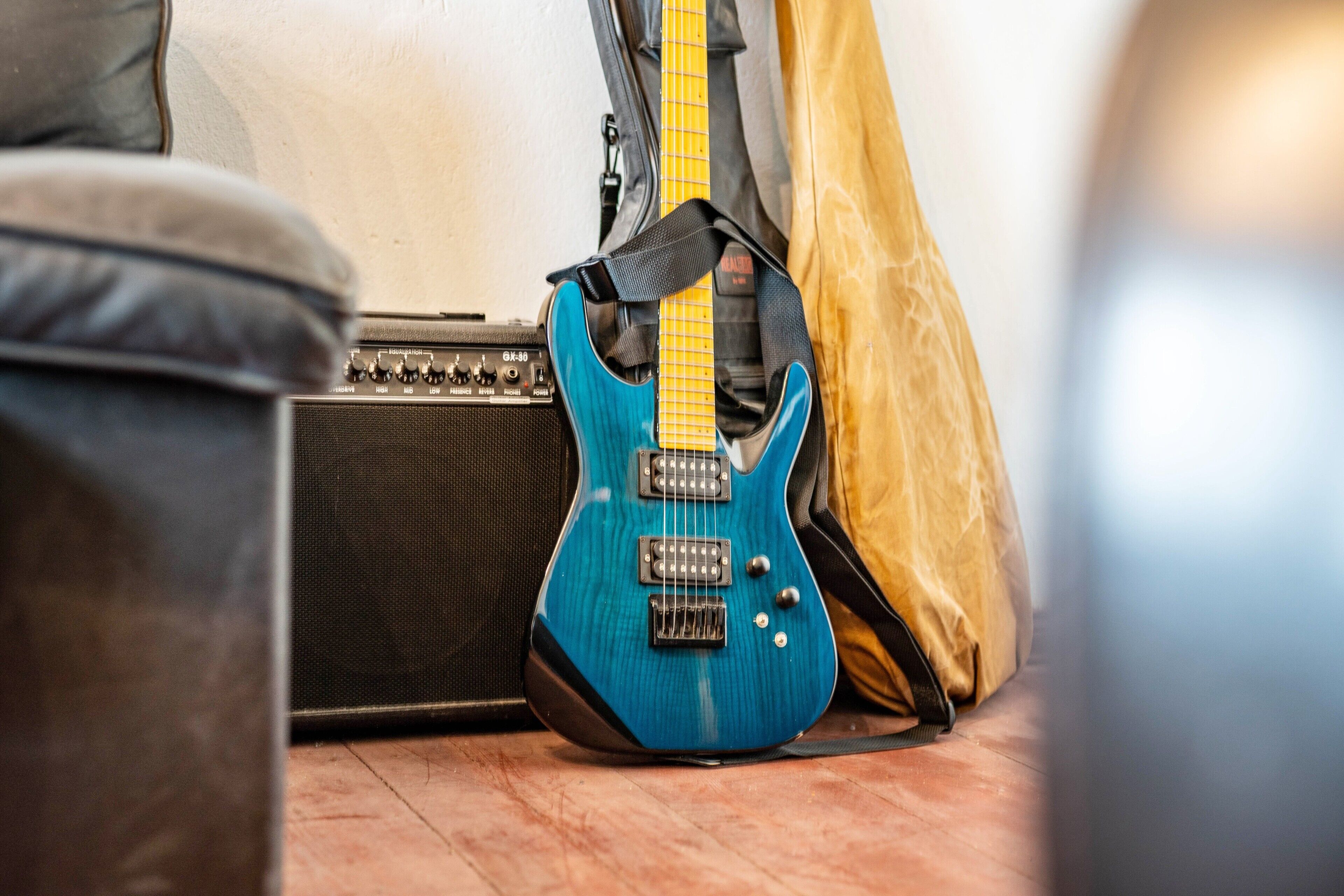 Une guitare électrique bleue, un amplificateur noir et une housse de guitare jaune sur un plancher en bois.
