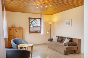 Un salon chaleureux avec un plafond en bois, un canapé, un fauteuil, une petite table et un meuble.