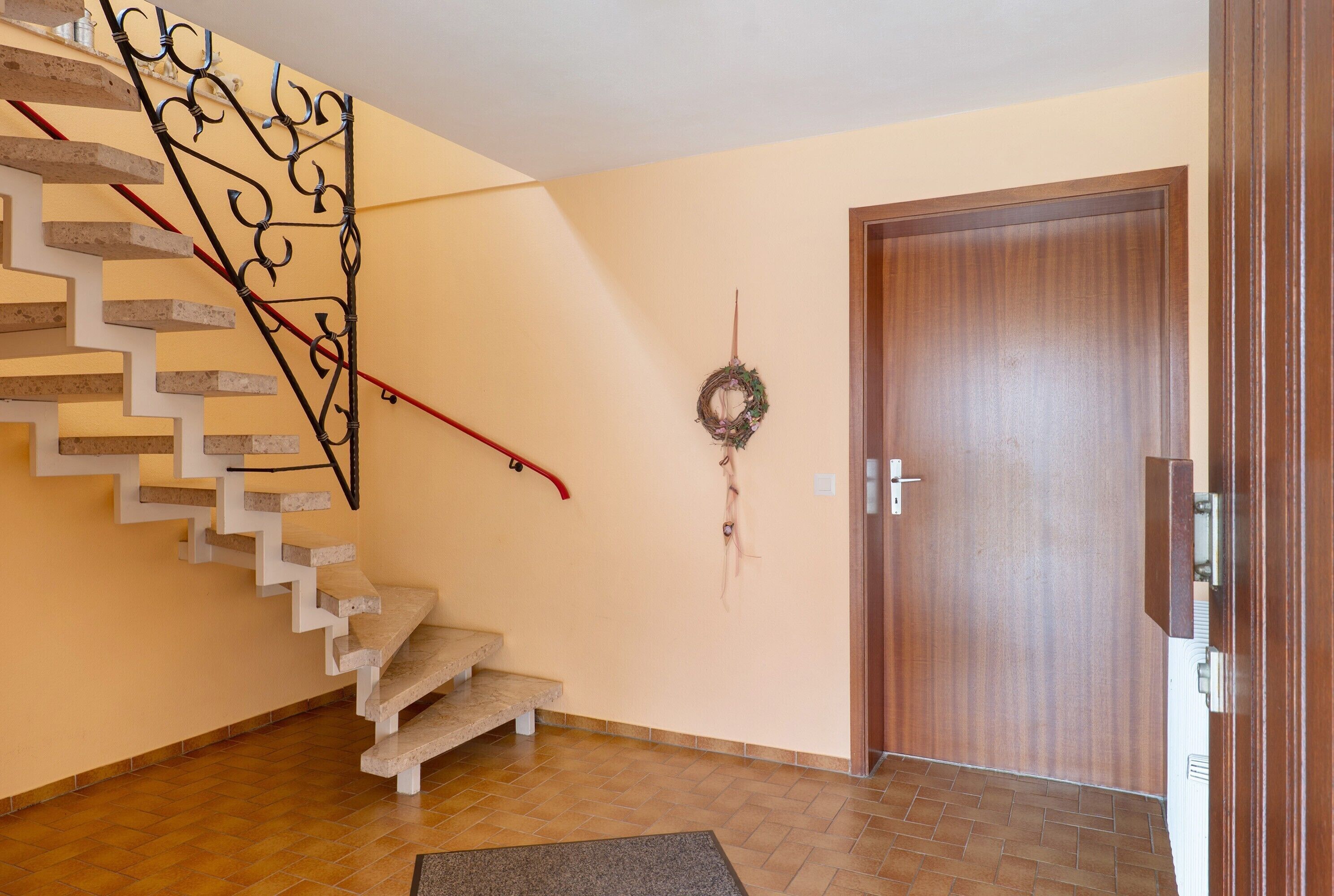 A staircase with a metal railing, a wooden door, and a wall-mounted wreath.