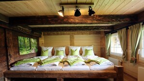 Dormitorio de cabaña de madera con una cama grande, vigas de madera y vista al bosque.