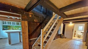 Una habitación amplia con una escalera de madera, una zona de cocina y un baño.