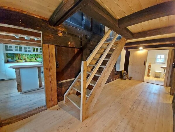 Una habitación amplia con una escalera de madera, una zona de cocina y un baño.