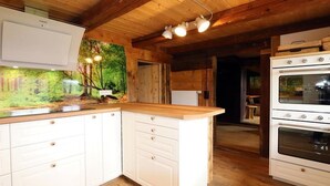 Una cocina con armarios de madera, horno empotrado y un cuadro con un paisaje forestal.