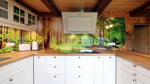 Una cocina con armarios blancos, encimera de madera y un mural con motivos forestales en la pared.