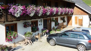 Un edificio tradicional con un balcón decorado con macetas colgantes de flores, un banco de madera y un coche estacionado.