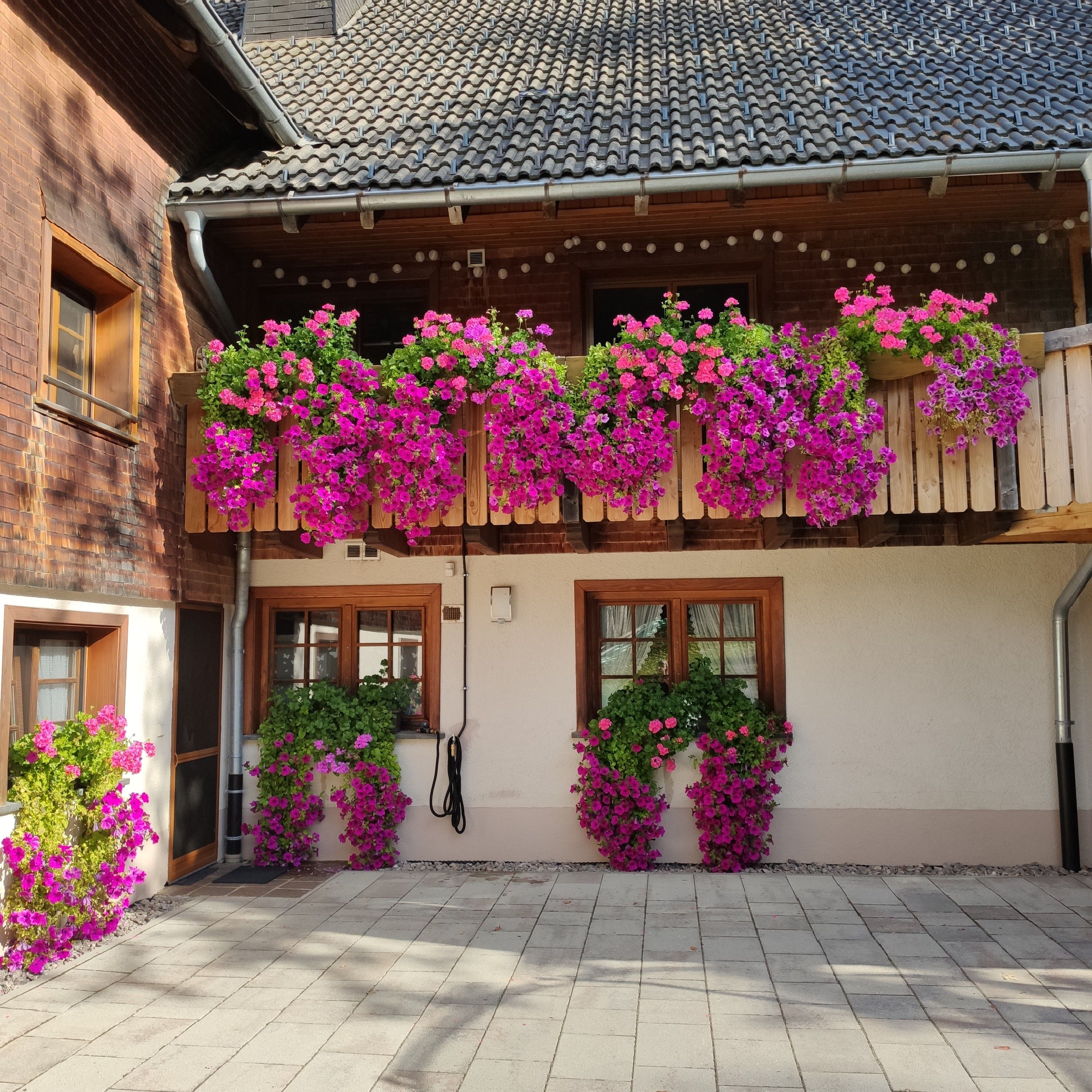 Ein Gebäude mit einem Ziegeldach, Holzbalkonbrüstungen und Blumenk ästen mit rosa Blüten.