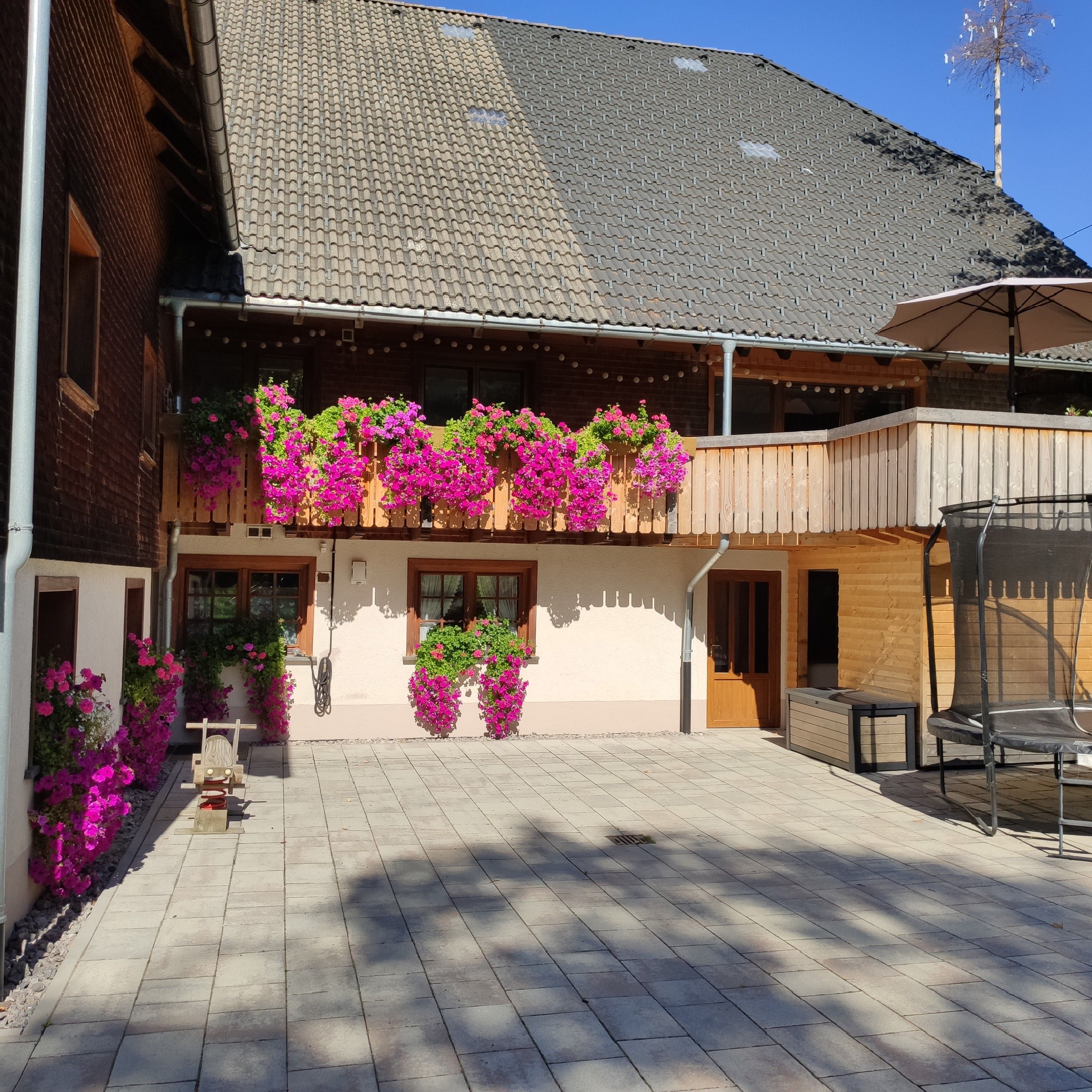 A building with a tiled roof, a balcony with hanging flower baskets, and a paved courtyard.