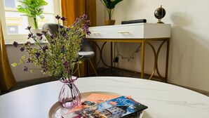 Ein Tisch mit Blumen, ein Tablett mit Zeitschriften, ein weißer Schreibtisch und eine Pflanze im Hintergrund.