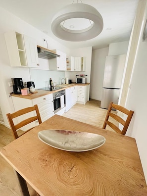 A modern kitchen with white cabinetry, a wooden dining table, and a built-in oven.