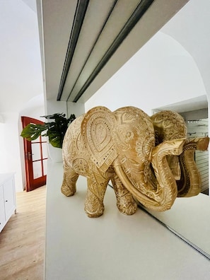 A room with a white wall, a plant, and a decorative elephant sculpture.