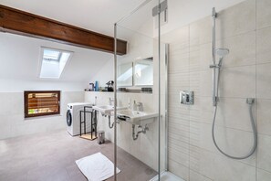 Ein modernes Badezimmer mit Duschkabine aus Glas, einer integrierten Waschmaschine und einem Oberlicht.