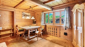 L’intérieur d’un chalet en bois, avec une table à manger, des chaises, un radiateur et une fenêtre avec des rideaux.