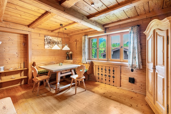 L’intérieur d’un chalet en bois, avec une table à manger, des chaises, un radiateur et une fenêtre avec des rideaux.