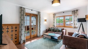 Un salon avec une table basse en bois, un canapé marron, un téléviseur et une fenêtre avec des rideaux.