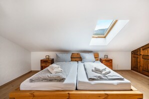 Une chambre avec un puits de lumière, deux lits, une tête de lit en bois, des tables de chevet et une armoire.